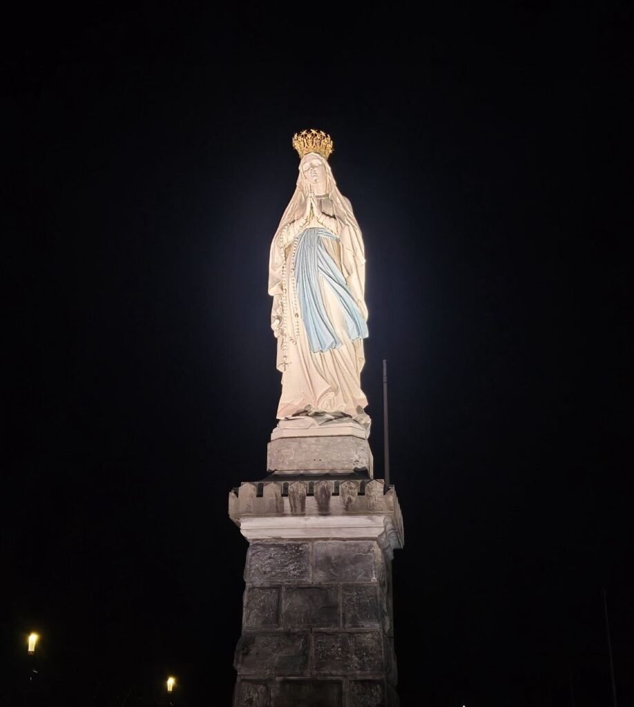 Crowned Virgin statue illuminated at night in Lourdes